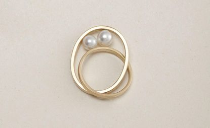 Two entwined gold rings with two oyster pearls sitting between the rings.