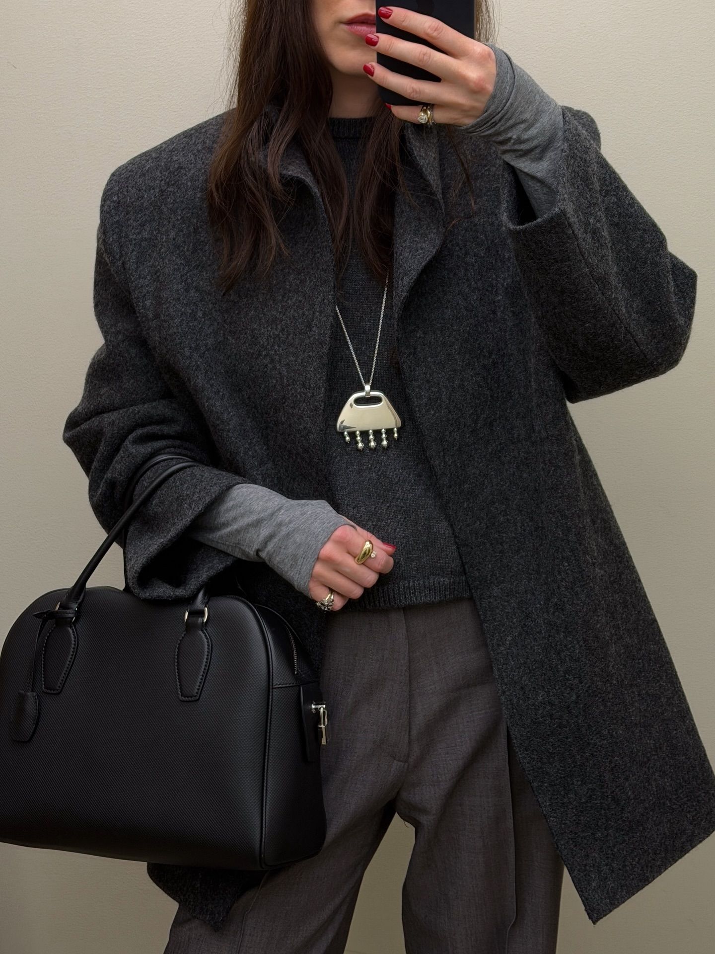 Woman wears grey coat, grey top, grey tailored trousers, black handbag