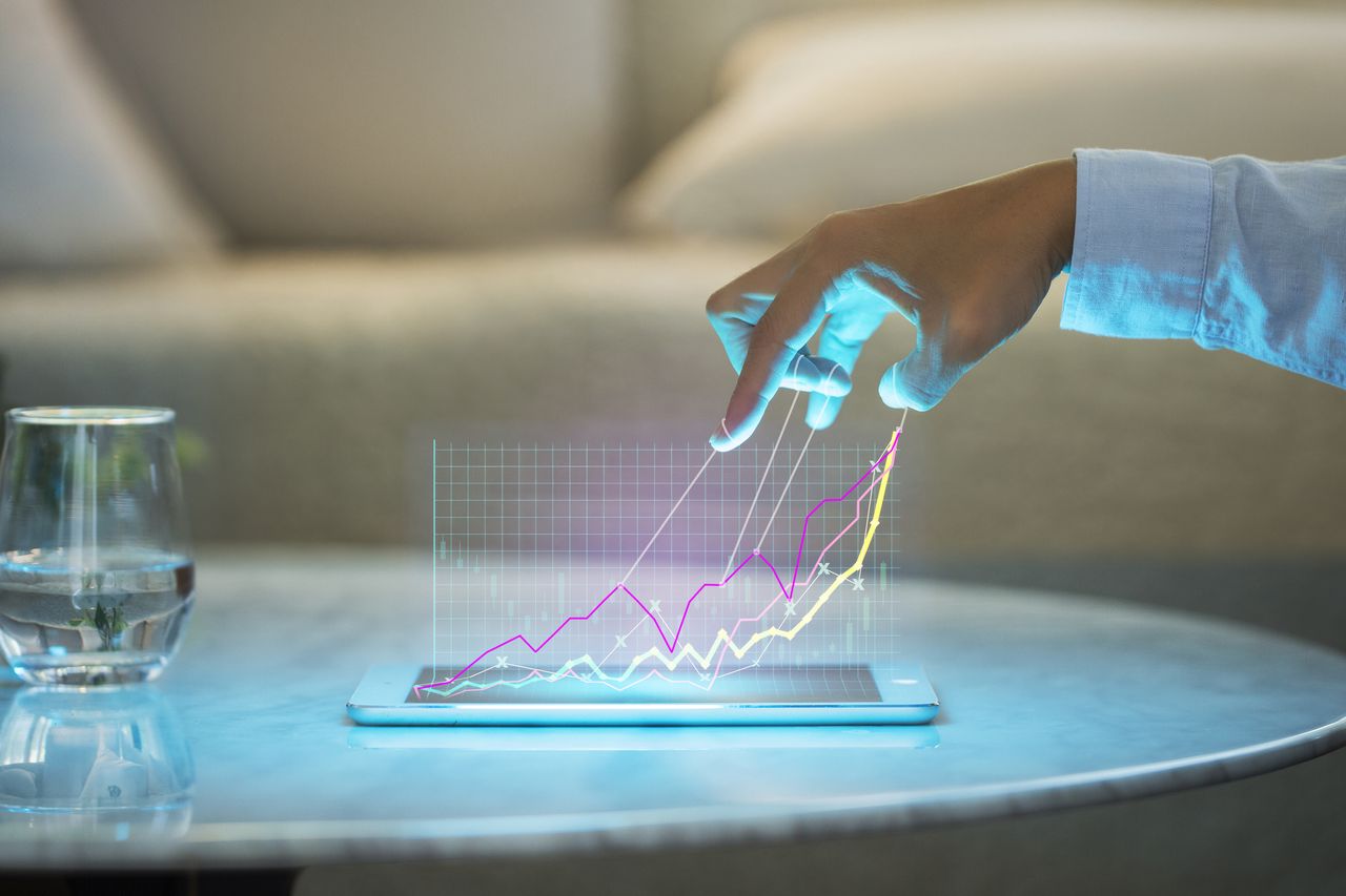 Investing graph image above a tablet, beneath a person&#039;s hand