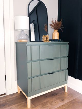 dark green cabinet in an entryway with a mirror on top
