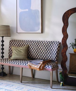 entryway with decorative upholstered bench with throw and cushion, stone floor tiles, rug, floor lamp, large mirror leaning up against wall, artwork