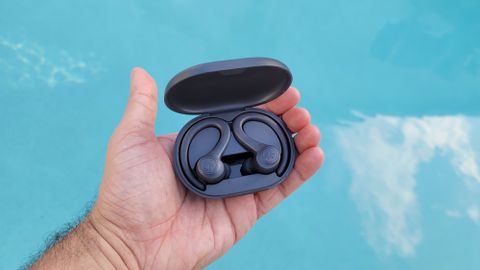 The JLab Go Air Sport wireless earbuds being held aloft a pool backdrop
