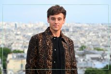 Tom Daley poses for a photo in a leopard print jacket with a view of Paris in the background