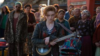 Sadie Sink's O'Dessa holding a guitar in front a crowd in O'Dessa