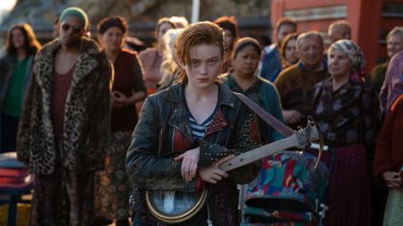 Sadie Sink's O'Dessa holding a guitar in front a crowd in O'Dessa