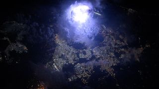 a bright flash of lighting as seen from orbit illuminates a city at night