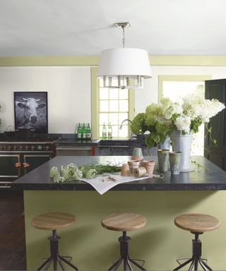 A kitchen with light green kitchen island with floral decor and round wooden bar stools