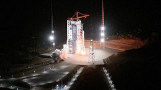 a rocket launches at night next to a launch tower