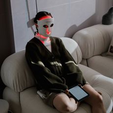 A woman sitting on a sofa wearing an LED mask