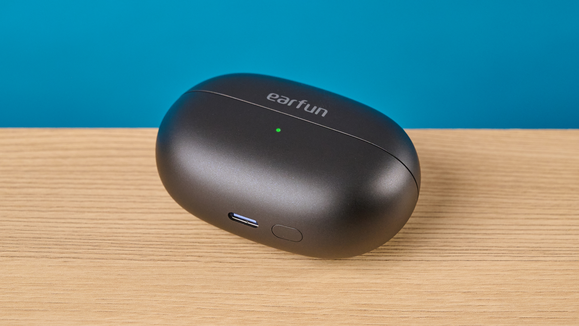 EarFun Clip 2 in black on table photographed in front of a blue background