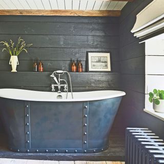 bathroom in Cotswolds cottage with large cast-iron bath with dark gunmetal exterior and white interior, with grey wood panel walls