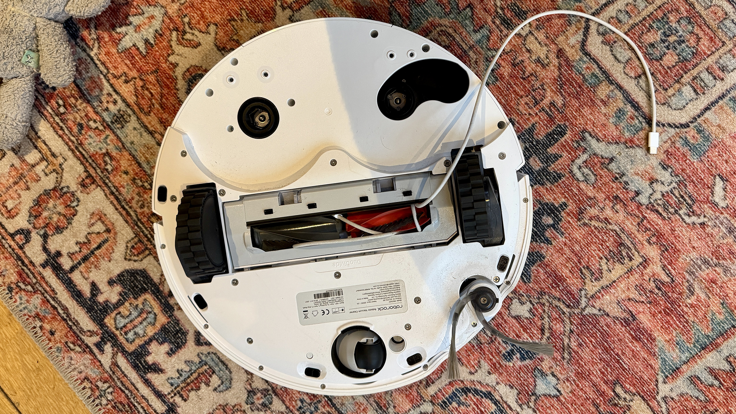 Roborock Qrevo Curv 2 Pro avoiding obstacles including a wire and dog toys, on a patterned rug