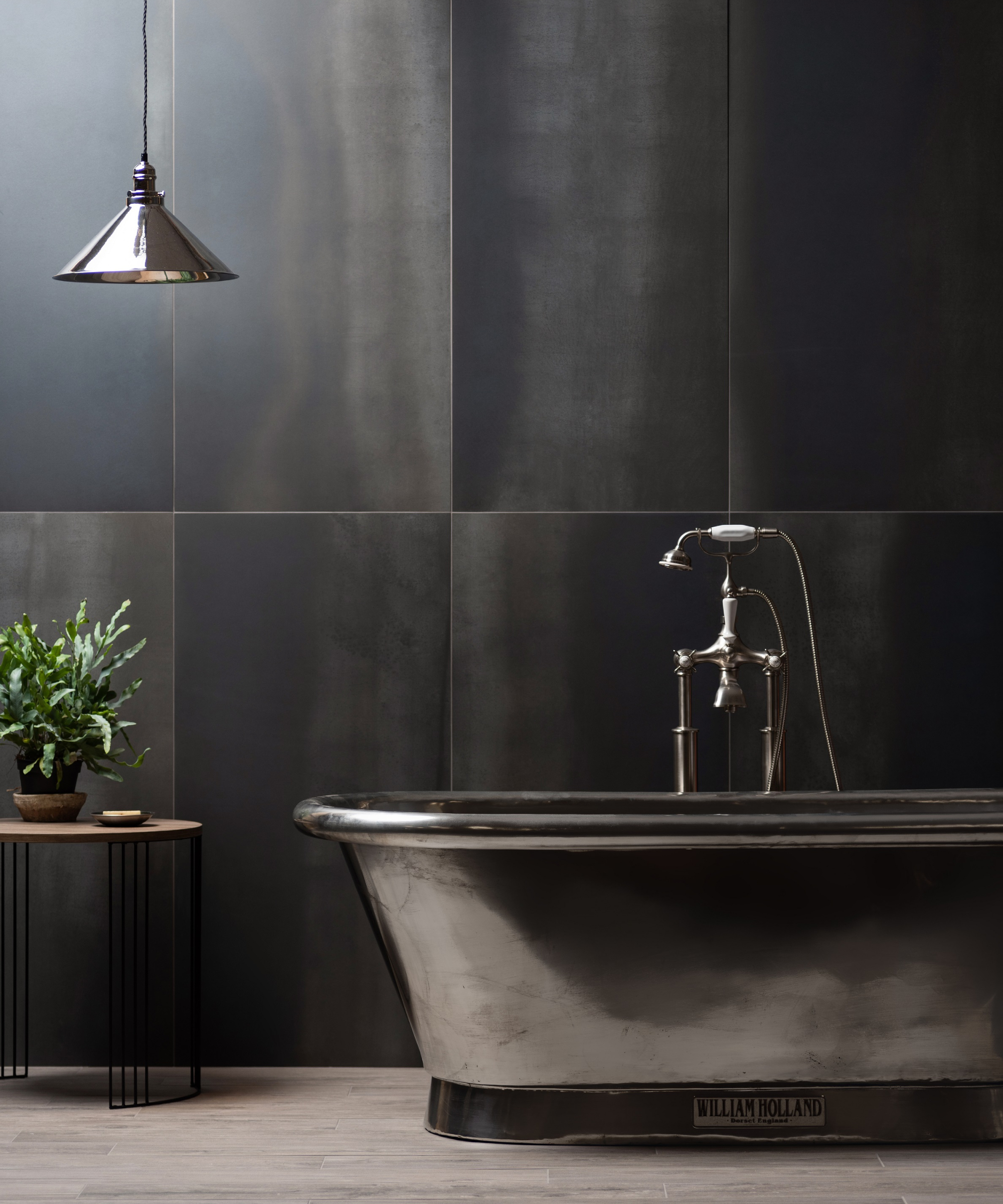 bathroom with black tiled walls, silver bath, pendant light and grey wooden effect flooring tiles