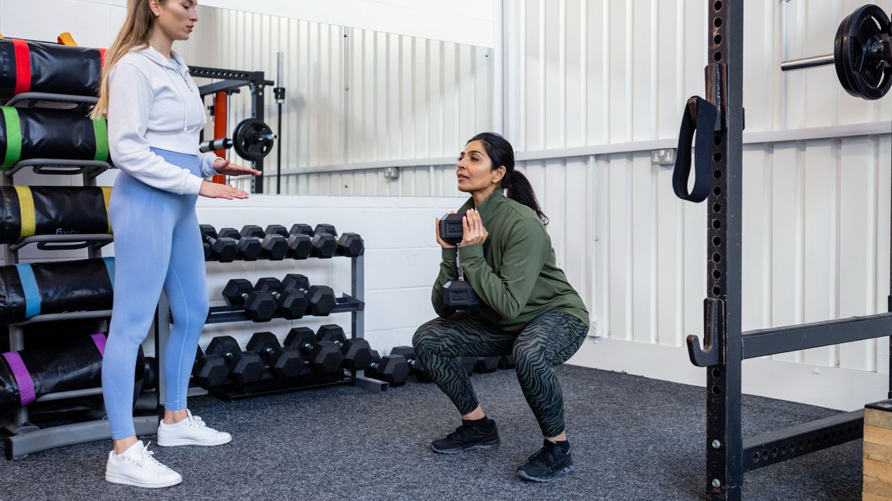 A coach teaching a client how to squat with a dumbbell