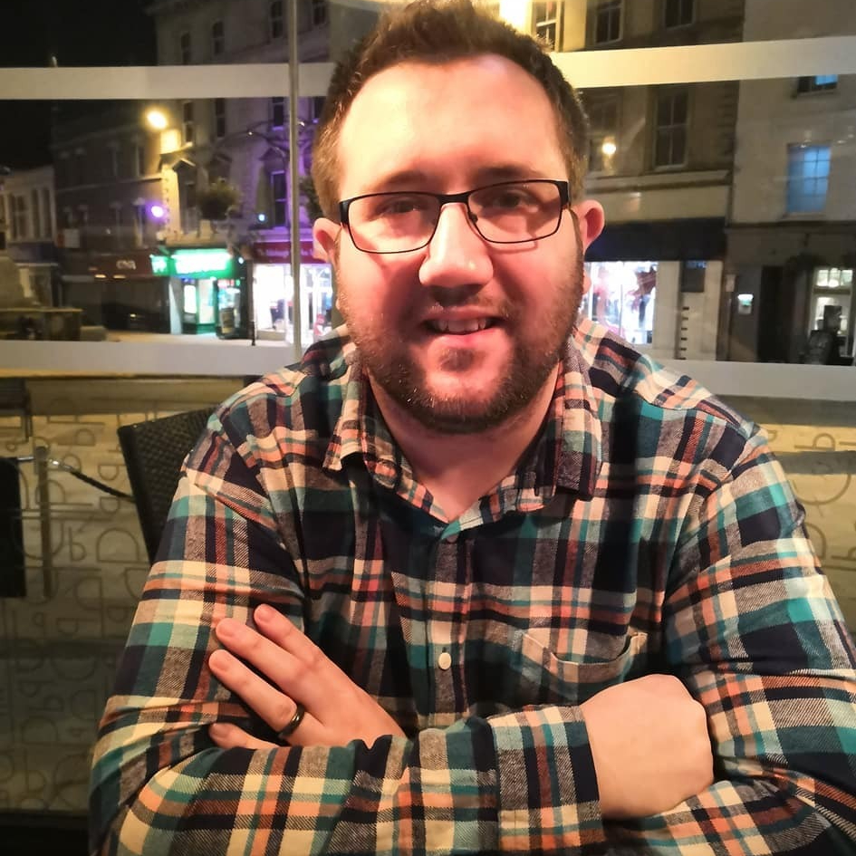 headshot of male with short hair and facial hair wearing check shirt