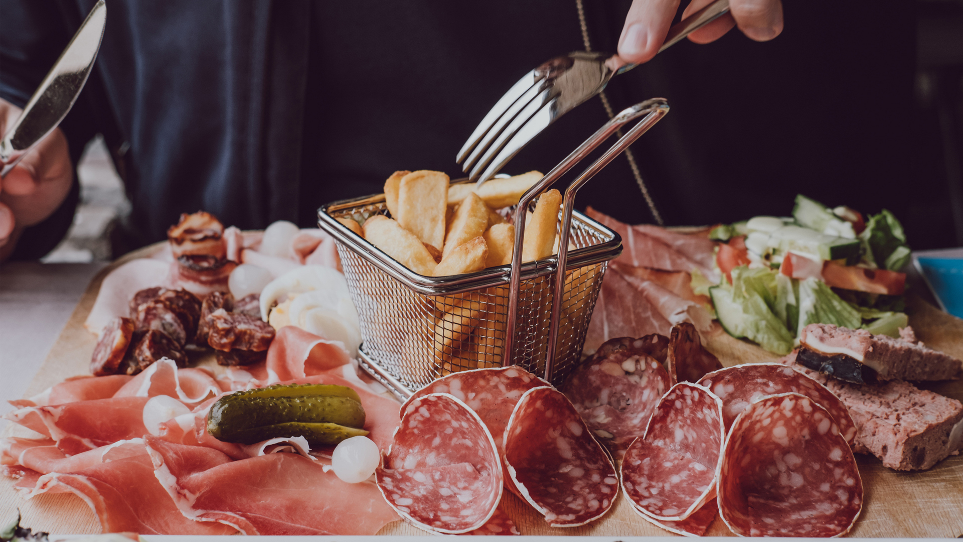 Man eating a plate of cured meat and french fries