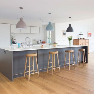 A white kitchen with a large grey island with wooden bar stools and statement lights above