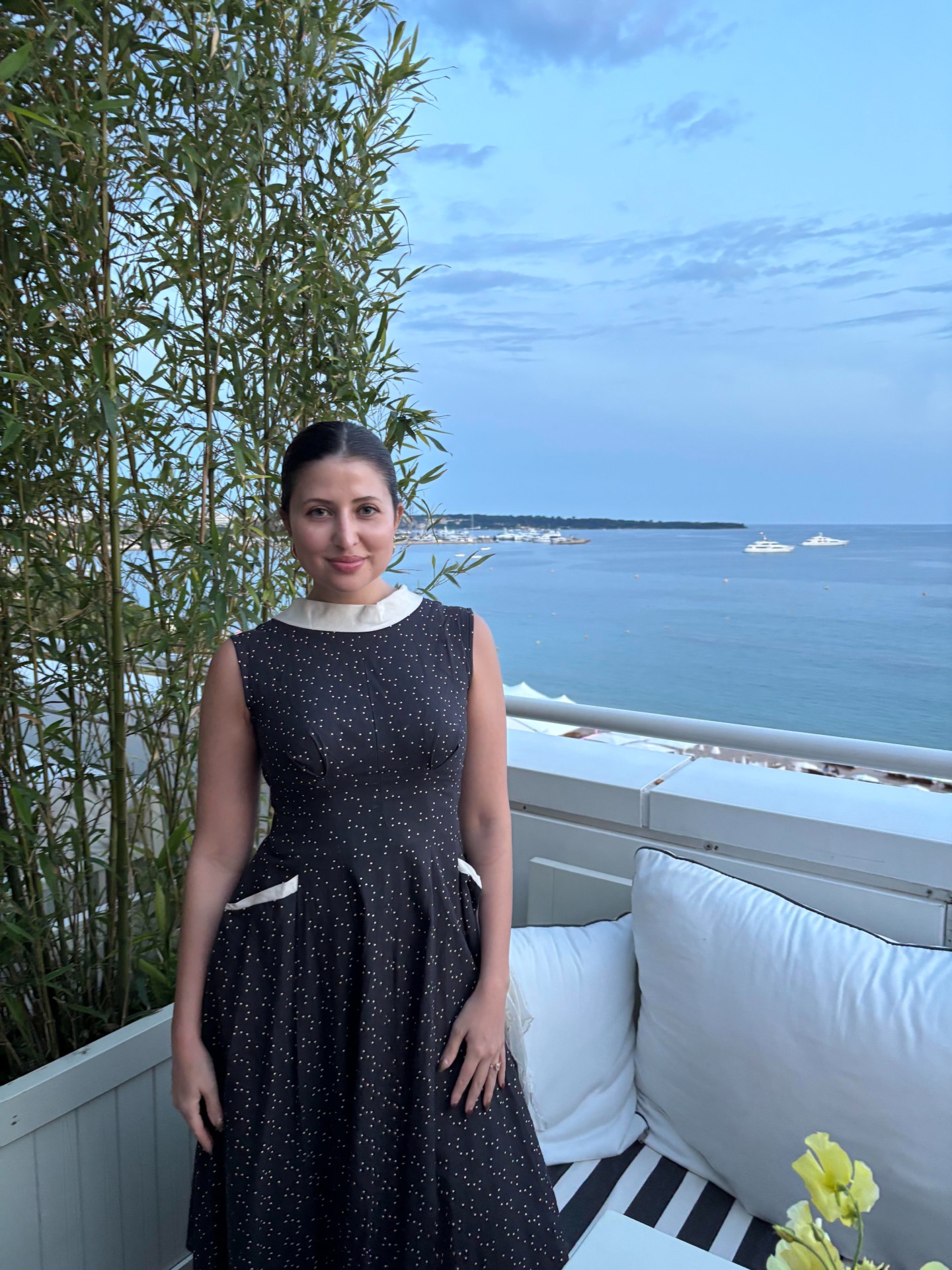 a woman in a black and white dress on a balcony in front of a white couch and the ocean in the background