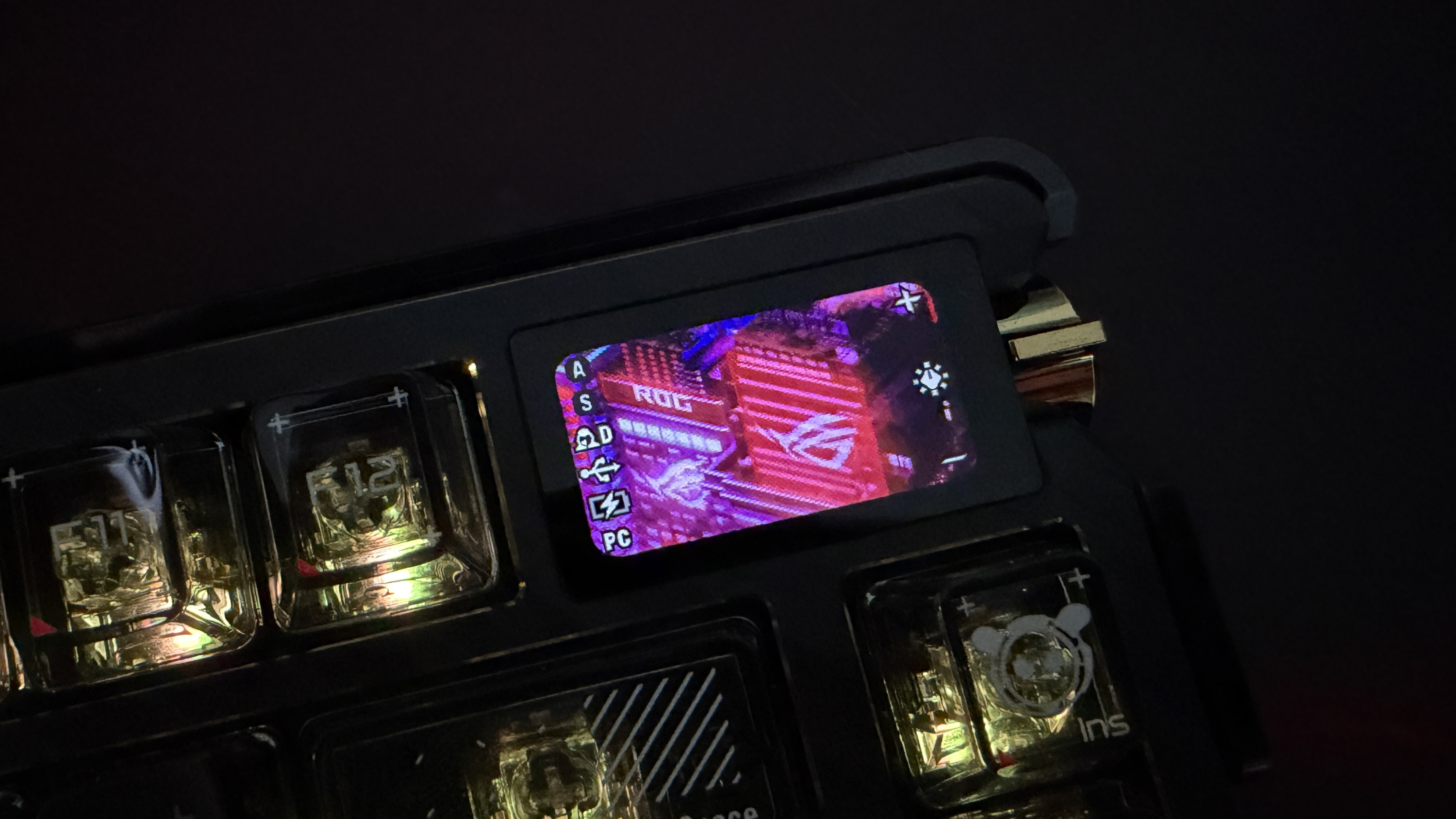 ASUS ROG mechanical keyboard with a small OLED screen showing the ROG logo and interface icons.