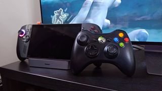 Black Xbox 360 controller leaning against ROG Xbox Ally X on Baseus Steam Deck dock.