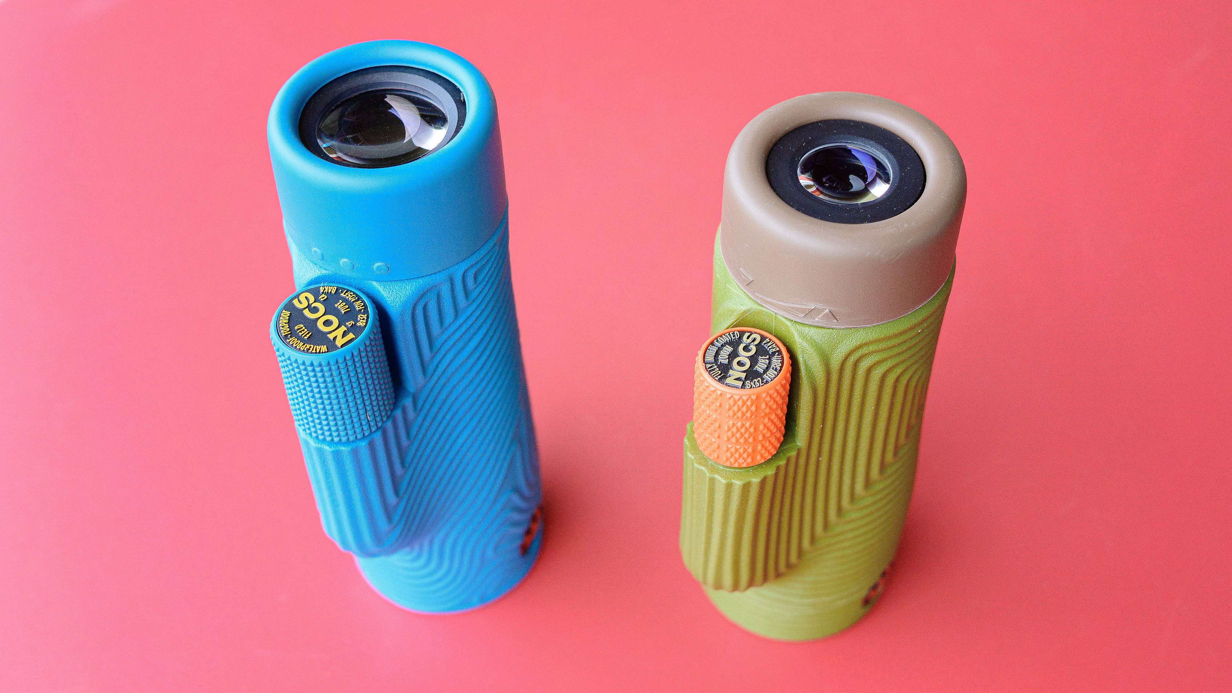 Nocs Field Tube monocular in blue.  Shown on a red table next to its predecessor, the Nocs Zoom Tube, which looks the same except it is dark green and orange.