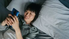 Woman using the best sleep apps on phone, smiling and lying down in bed