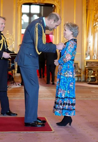 Prince William wearing a military uniform bending over to give Imelda Staunton, wearing a blue floral dress, a damehood medal