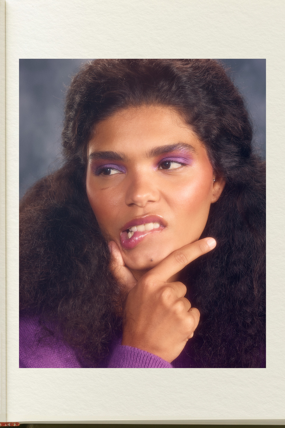 A model posing with her fingers on her chin, wearing purple eyeshadow