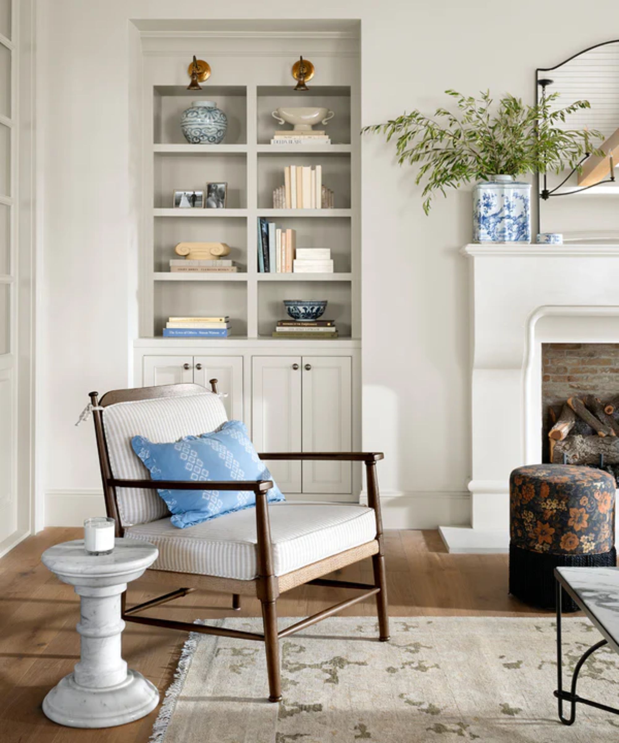 a chair with striped cushions and a blue pillow, a pedestal table next to the chair, a rug on the floor, and a built in bookcase behind the chair