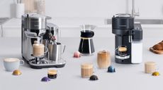 White counter with two Nespresso coffee machines on it surrounded by cups of coffee and pods