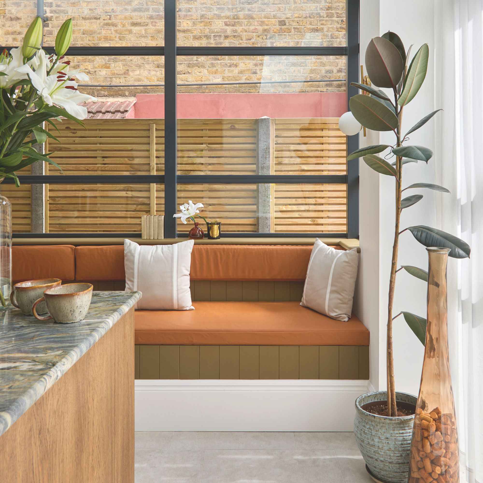 Kitchen seating area with built-in banquette seating with orange cushions and a plant next to it