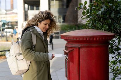 Happy woman in London posting a letter in the mailbox