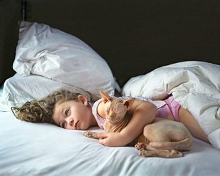 A girl lying in a bed holding a brown cat.