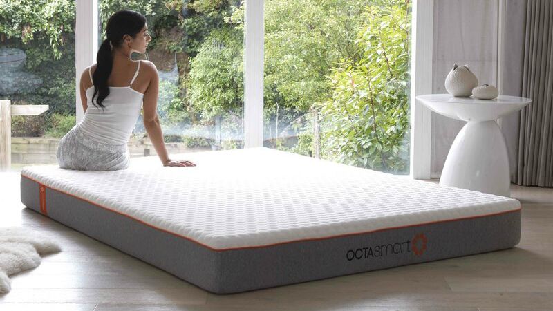 Best Dormeo mattress sales and discount codes: A woman with long dark hair sits on the Dormeo Octasmart Hybrid mattress