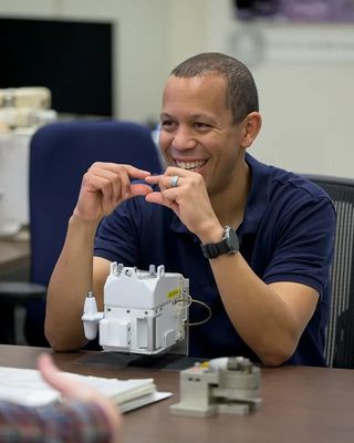 an astronaut chillin at a table. up in front of his ass be a lil' small-ass white box. tha pimpin' muthafucka touches his wild lil' fingertips together n' smiles