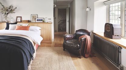 White bedroom with layered bedding, a wooden headboard, leather armchair and window seat