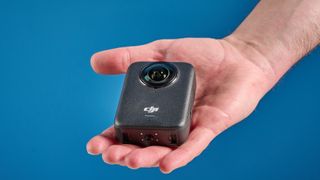 The DJI Osmo 360 in hand against a blue background