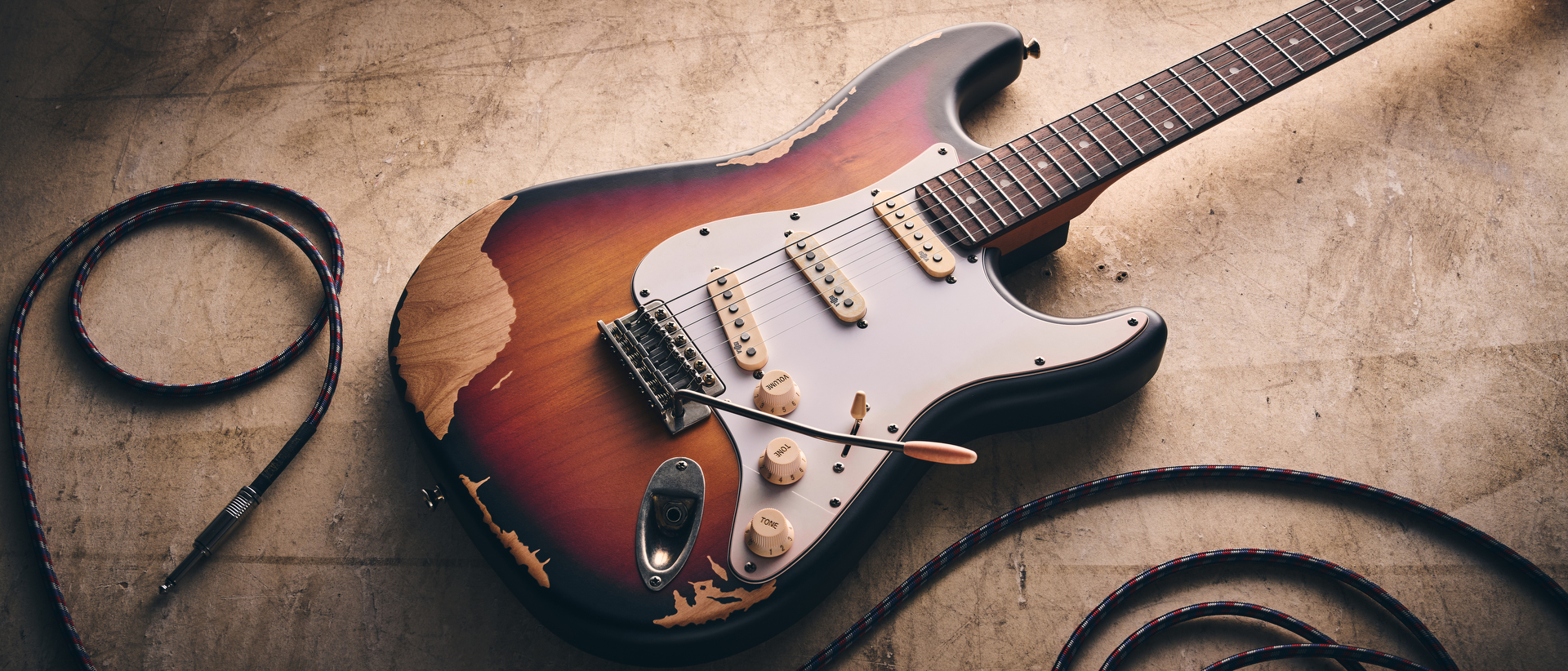 A Harley Benton ST-62HA electric guitar on a concrete floor with a guitar cable