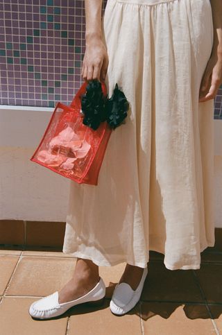 a woman stands with a red mesh bag and a linen skirt from the jcrew x maryam nassir zadeh collaboration