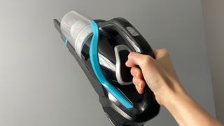 The Bissell CleanView Pet Slim Cordless Stick Vacuum being used in handheld mode to clean up high with a grey wall at the back