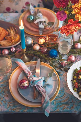 Overhead view of a table laid with colourful plates, Christmas baubles and lit candles.
