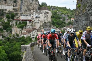 Team Visma - Lease a Bike team's Danish rider Jonas Vingegaard (C) and UAE Team Emirates team's Slovenian rider Tadej Pogacar wearing the overall leader's yellow jersey (rear R) cycle with the pack of riders (peloton) past the town of Rocamadour during the 12th stage of the 111th edition of the Tour de France cycling race, 203,6 km between Aurillac and Villeneuve-sur-Lot, southern central France, on July 11, 2024. (Photo by Marco BERTORELLO / AFP)