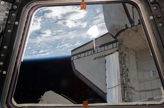 A portion of the docked space shuttle Endeavour appears through a Cupola window of the International Space Station. Earth's horizon and the blackness of space provide the backdrop for the scene on May 23, 2011 (Flight Day 8).