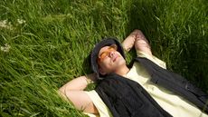 A man lies on his back in the grass with his eyes closed.