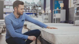 A man in a blue shirt goes mattress shopping during the best time of the year