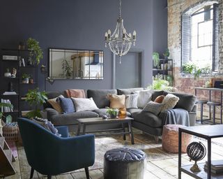 A dark blue living room with chandelier, L-shaped sofa, and horizontal full length mirror