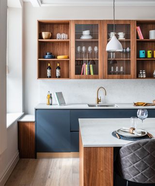 A modern kitchen with blue units, warm wood shelves and a stone-topped island