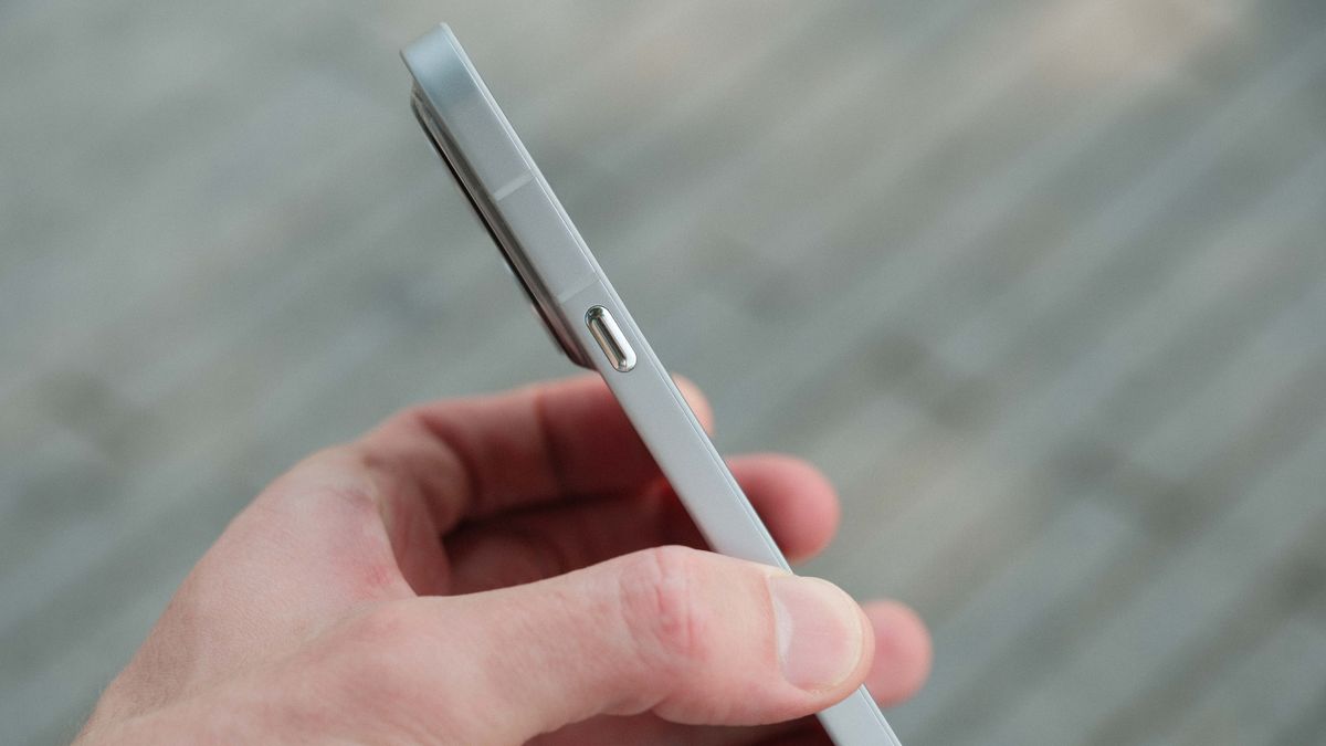 A side profile view of a light gray smartphone held in a hand. The image highlights the phone's flat edge, a thin antenna line, and a single metallic power button.