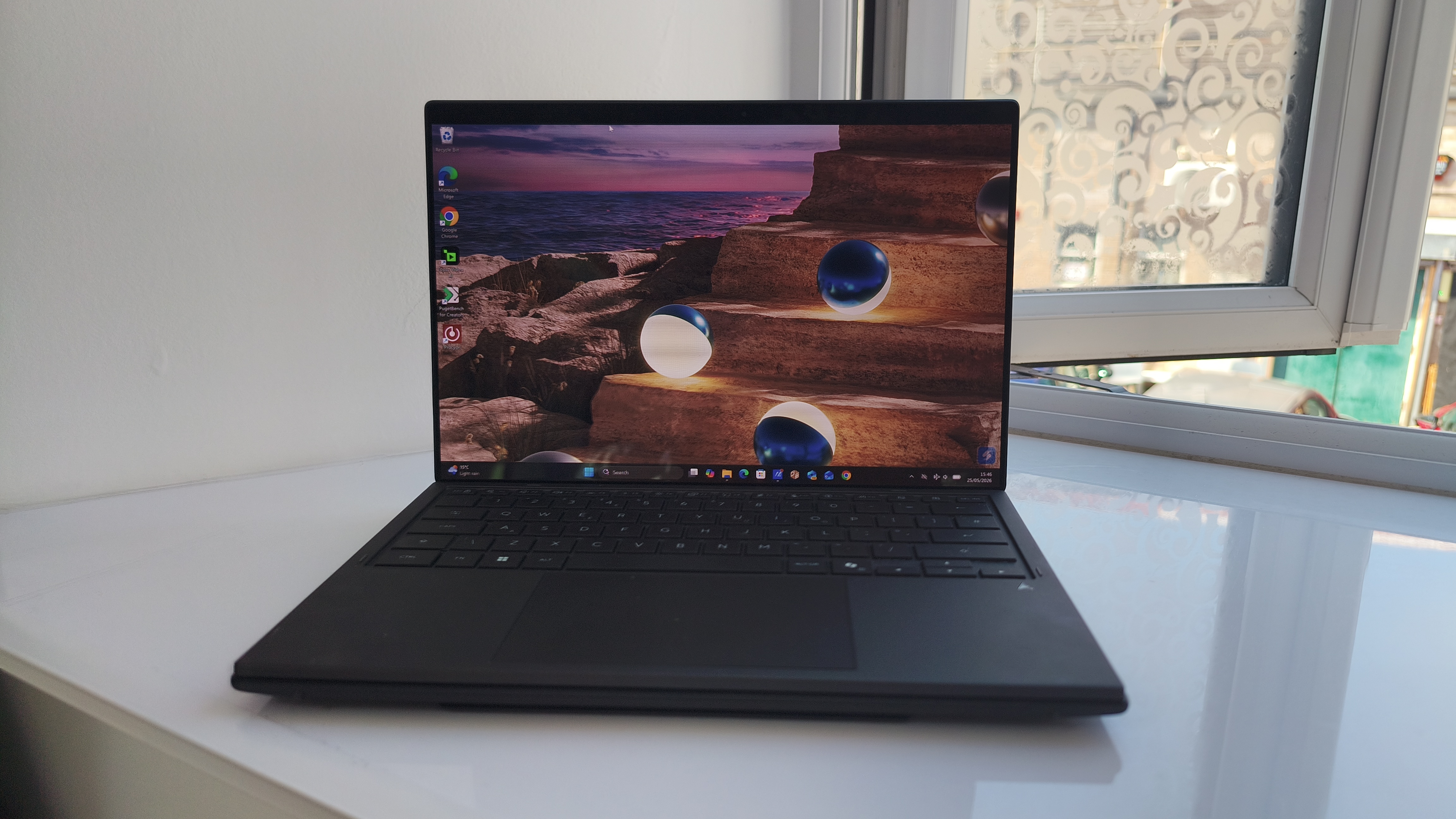 A front-on view of the ASUS Zenbook Duo sitting on a white counter in standard laptop mode, with the keyboard covering the lower display and the top screen showing a vibrant blue orb wallpaper.