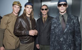 Four male models wearing clothing by Versace in brown shades.